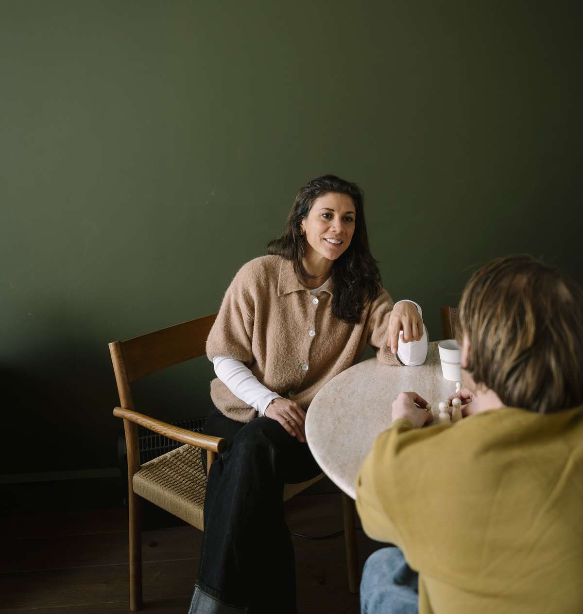 Iris in gesprek met een cliënt aan tafel voor een donkergroene muur