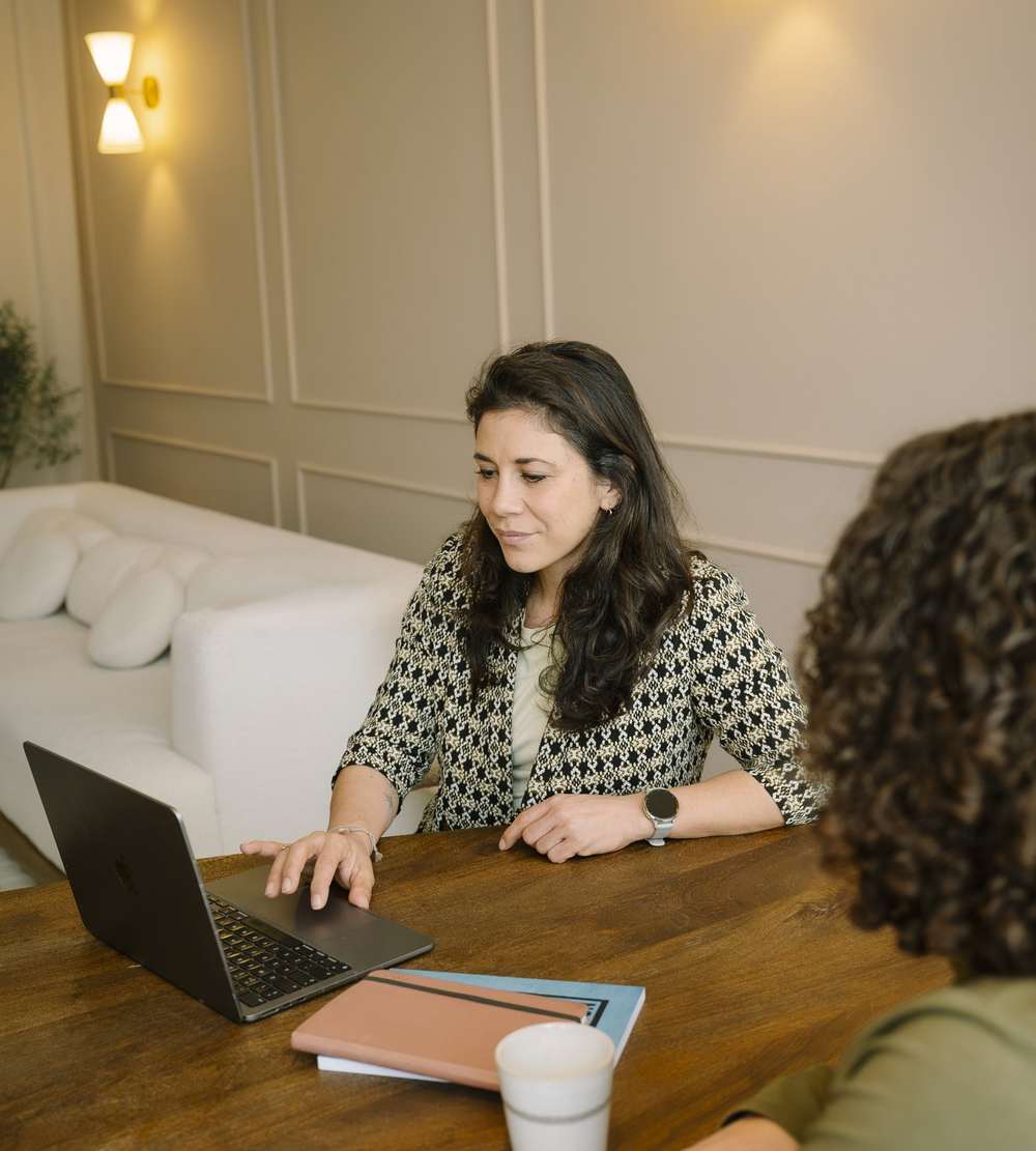 Iris aan tafel met haar laptop, in gesprek met een cliënt